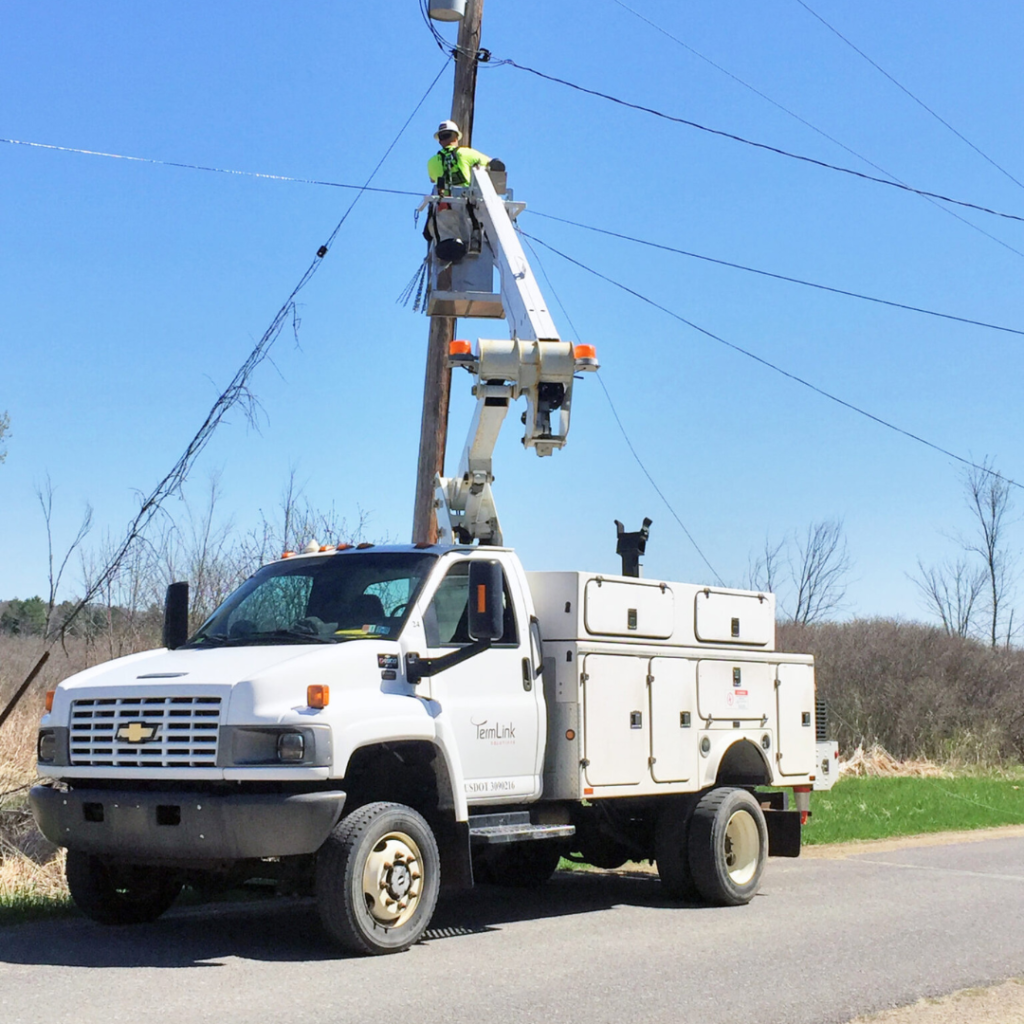 Fiber technicians wearing PPE working safely on a utility pole during aerial fiber installation