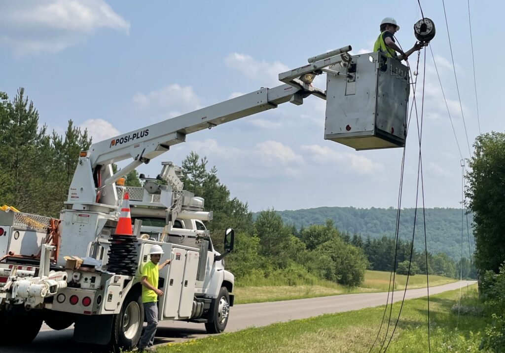 Crew performing aerial fiber installation project with bucket truck in rural setting